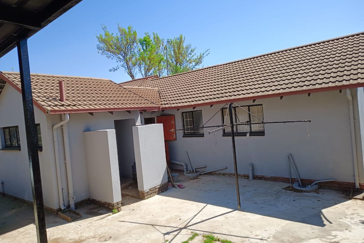 Rear exterior view of the house featuring a tiled roof, concrete patio area, and exposed external plumbing fixtures.
