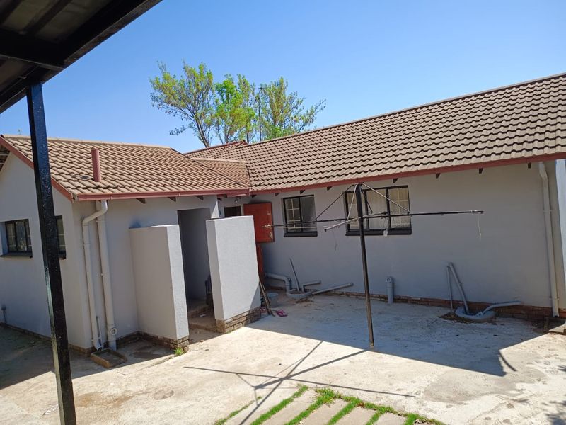 Rear exterior view of the house featuring a tiled roof, concrete patio area, and exposed external plumbing fixtures.