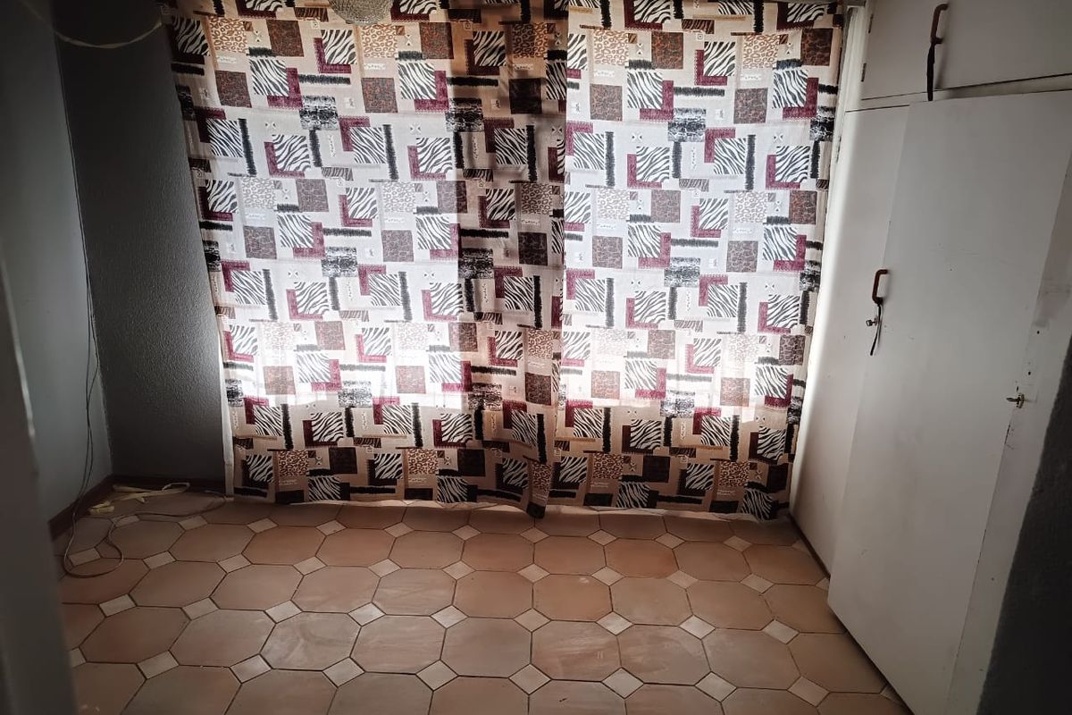 A simple bedroom featuring built-in cupboards and tiled flooring, offering a blank canvas for potential updates and interior design improvements.