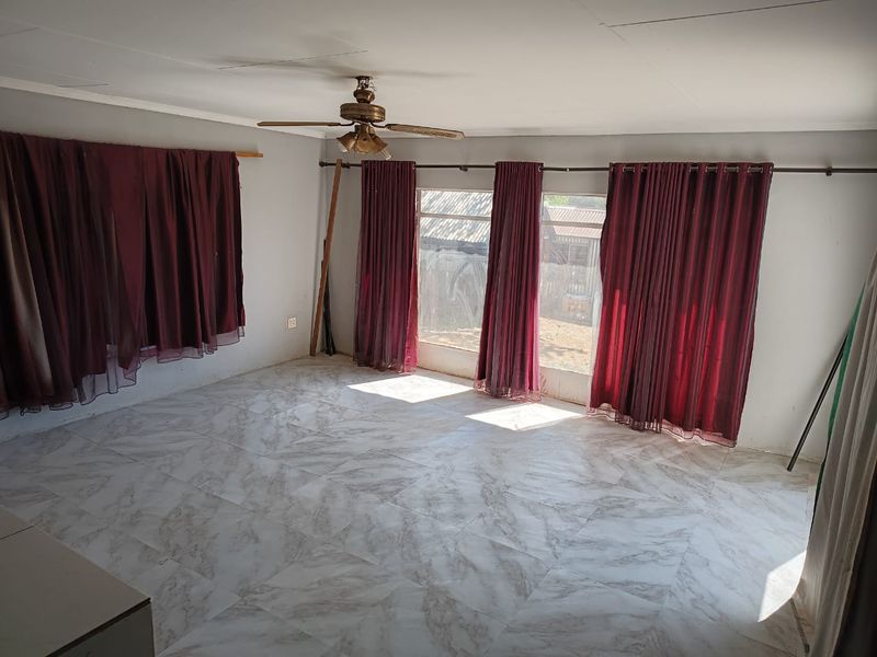 A spacious, empty living room featuring tiled flooring, a ceiling fan, and large windows with curtain rods, offering a blank canvas for interior design.