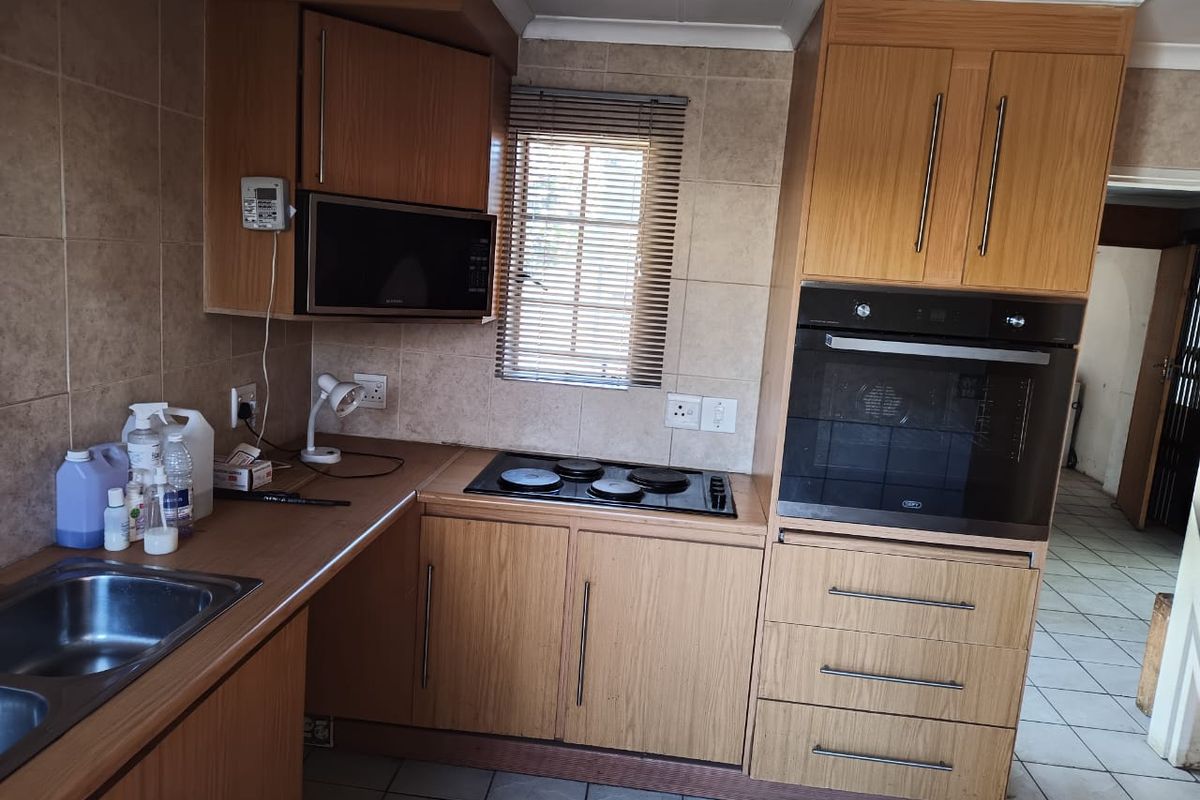 A functional kitchen featuring wood-finish cabinetry, built-in oven and hob, tiled backsplash, and tiled flooring, offering a practical layout for daily use.