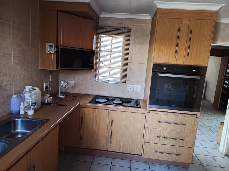 A functional kitchen featuring wood-finish cabinetry, built-in oven and hob, tiled backsplash, and tiled flooring, offering a practical layout for daily use.