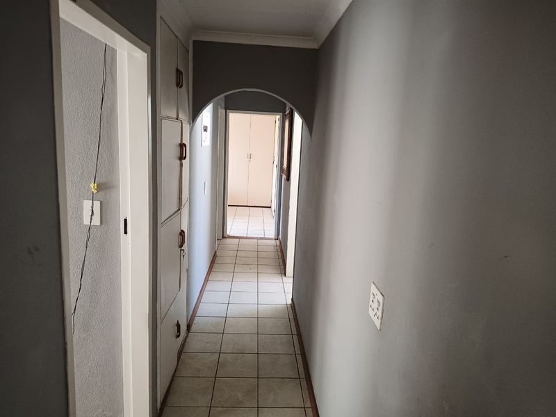 A functional hallway featuring tiled flooring, built-in storage cupboards, and a decorative archway leading to adjacent rooms.