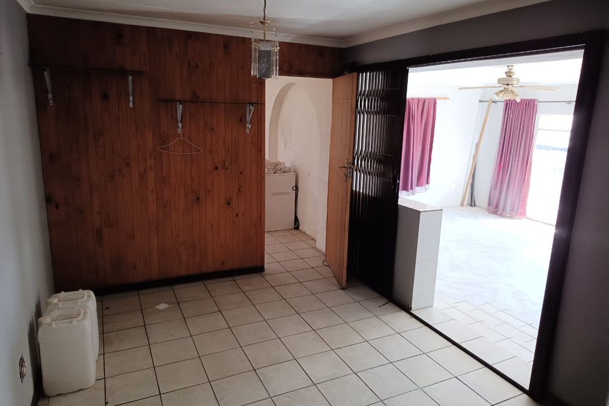 An empty living area featuring tiled flooring, wood-paneled walls, and a security gate leading to an adjacent room.