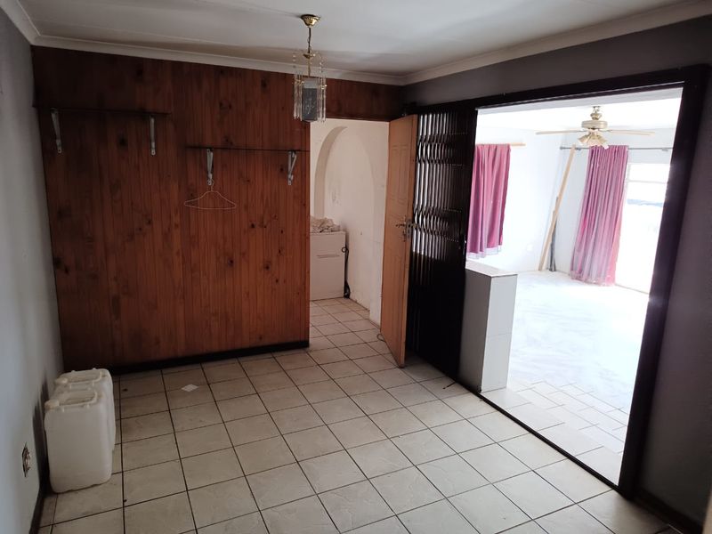 An empty living area featuring tiled flooring, wood-paneled walls, and a security gate leading to an adjacent room.