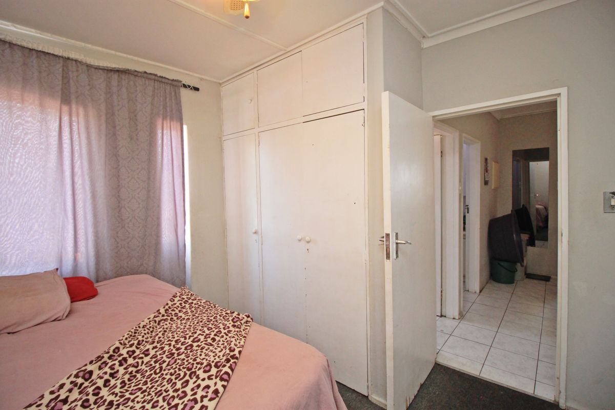 A bedroom featuring built-in cupboards and access to an adjacent hallway with tiled flooring.