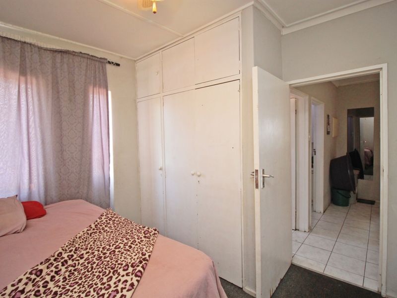A bedroom featuring built-in cupboards and access to an adjacent hallway with tiled flooring.