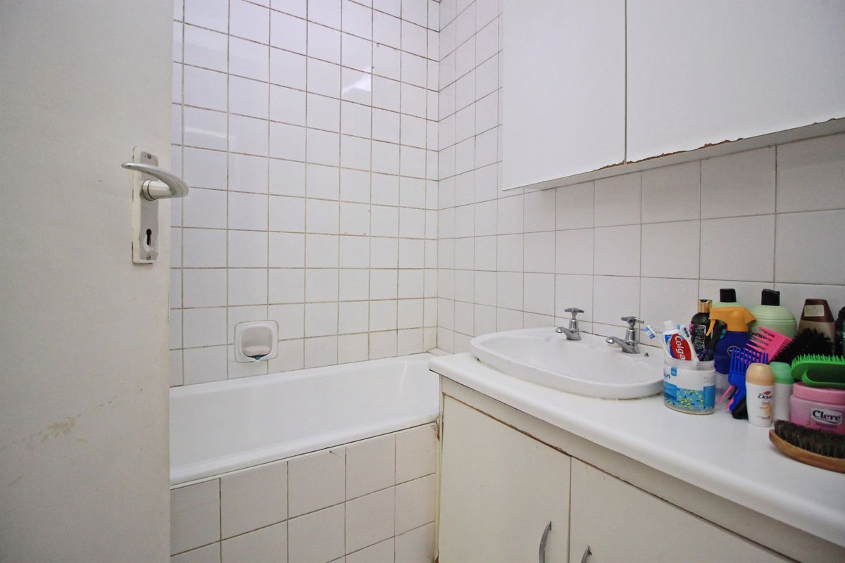 A compact bathroom featuring a built-in bathtub, vanity cabinet with washbasin, and wall-mounted storage, finished with white ceramic wall tiles.