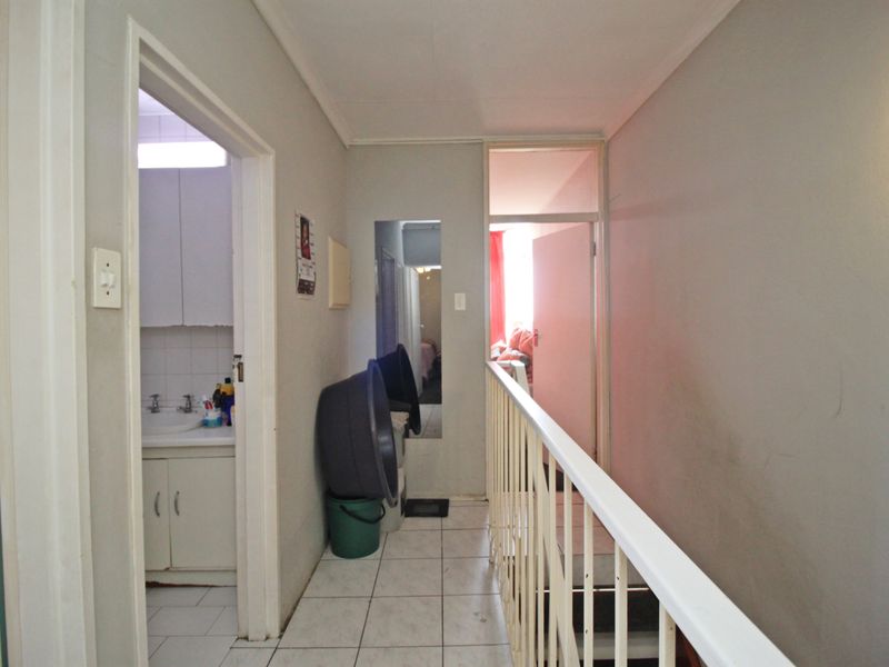 A functional hallway featuring tiled flooring and a metal balustrade, providing access to adjacent rooms and a bathroom area.