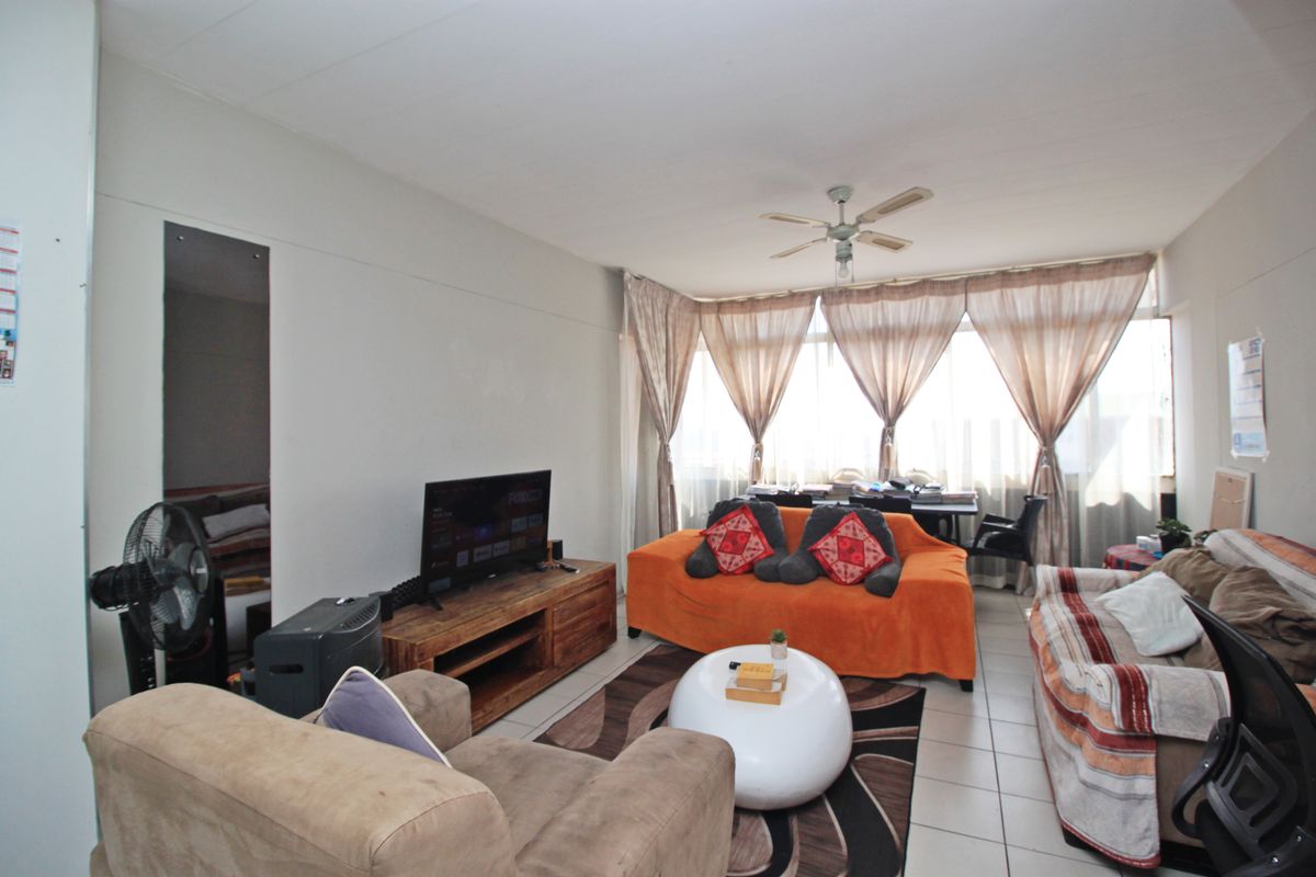 A living room area featuring tiled flooring, a ceiling fan, and a large window providing natural light.