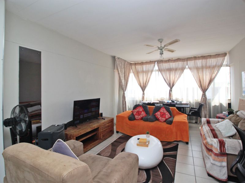 A living room area featuring tiled flooring, a ceiling fan, and a large window providing natural light.