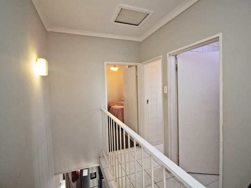 A functional upper-level hallway featuring tiled flooring, a metal balustrade, and access to adjacent bedrooms and bathroom areas.