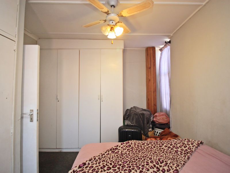 A bedroom featuring built-in cupboards, a ceiling fan, and a timber door frame, requiring cosmetic updates to improve its overall condition.