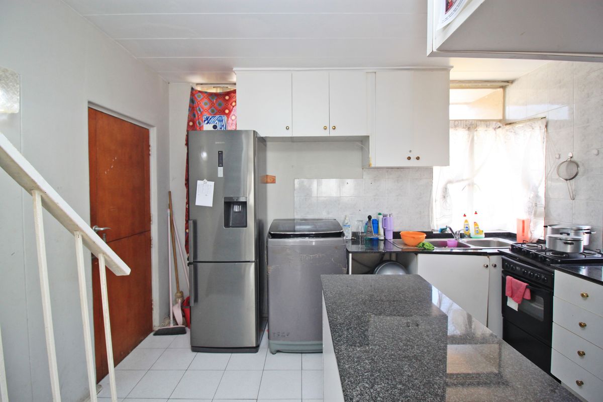 A functional kitchen featuring granite countertops, built-in cabinetry, a stainless steel oven and hob, and tiled flooring, adjacent to an internal staircase.