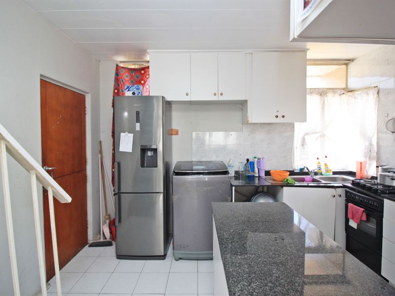 A functional kitchen featuring granite countertops, built-in cabinetry, a stainless steel oven and hob, and tiled flooring, adjacent to an internal staircase.