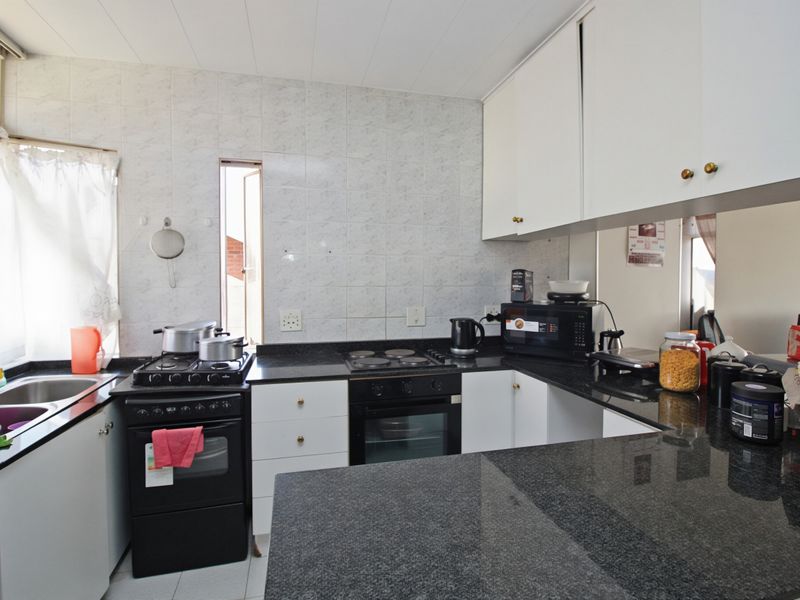 Functional kitchen featuring granite countertops, white cabinetry, and a built-in oven with electric hob, offering a practical layout for daily meal preparation.