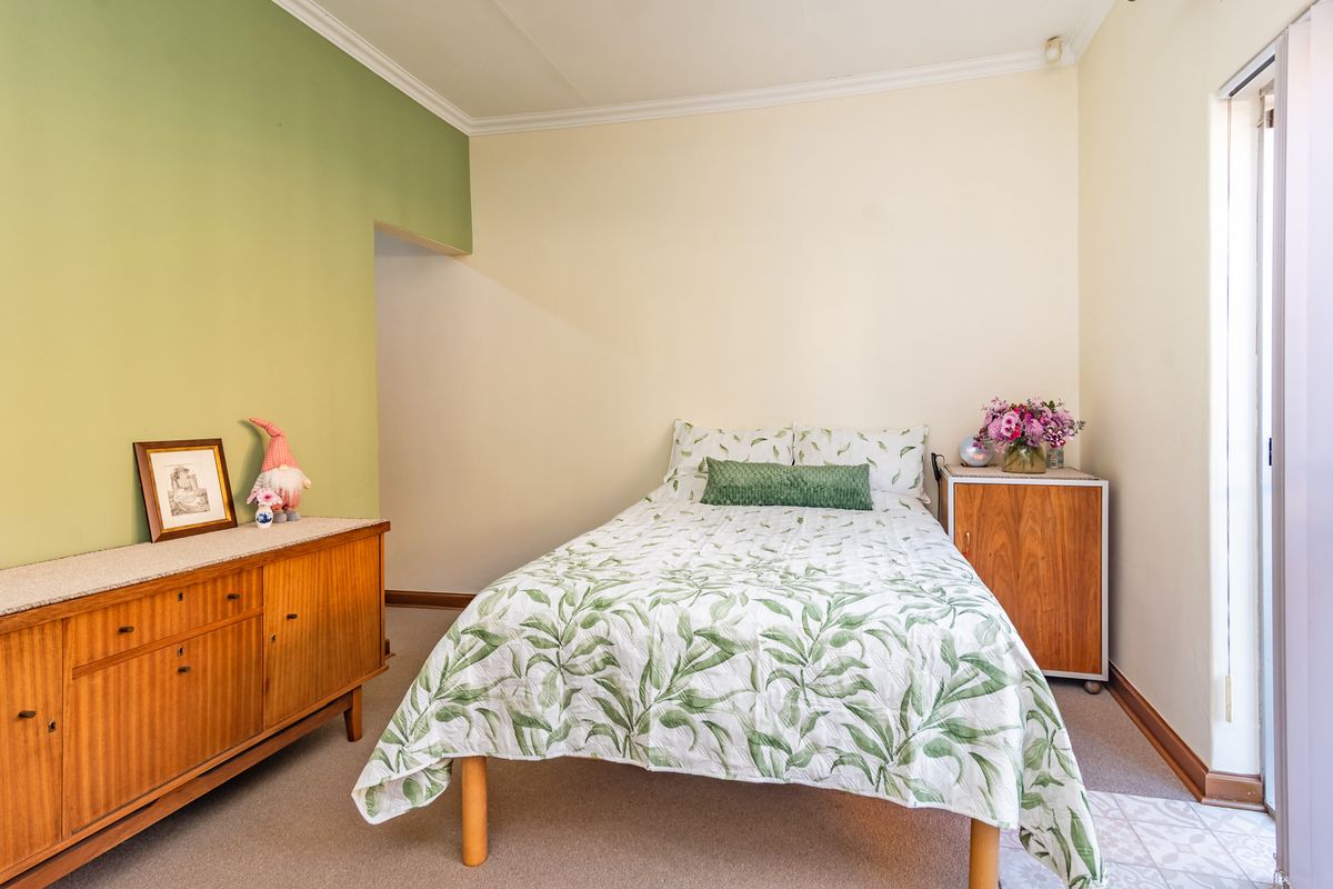 A well-lit bedroom featuring neutral walls with a green accent wall, crown molding, and carpeted flooring.