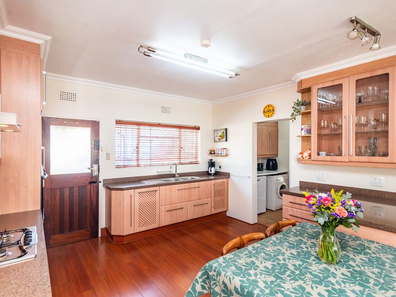 A functional kitchen featuring wooden cabinetry, laminate countertops, a gas hob, and timber flooring, with an adjacent scullery area visible.