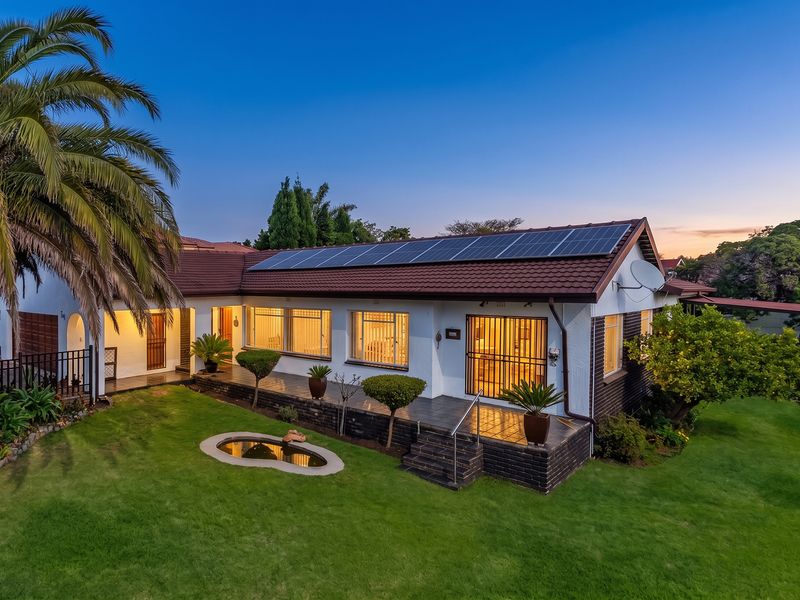 Rear view of a well-maintained house featuring a tiled roof with solar panels, a paved patio area, and a landscaped garden with a pond.