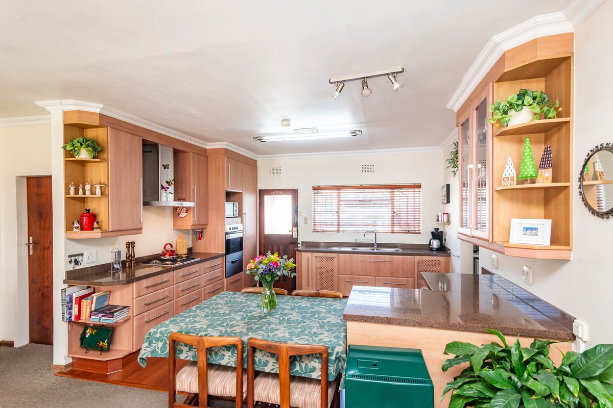 A functional kitchen featuring wood-finish cabinetry, granite countertops, built-in oven, gas hob, and a dedicated dining area with natural light.