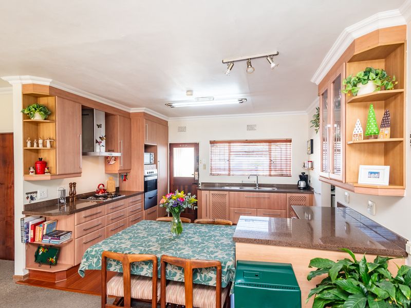 A functional kitchen featuring wood-finish cabinetry, granite countertops, built-in oven, gas hob, and a dedicated dining area with natural light.