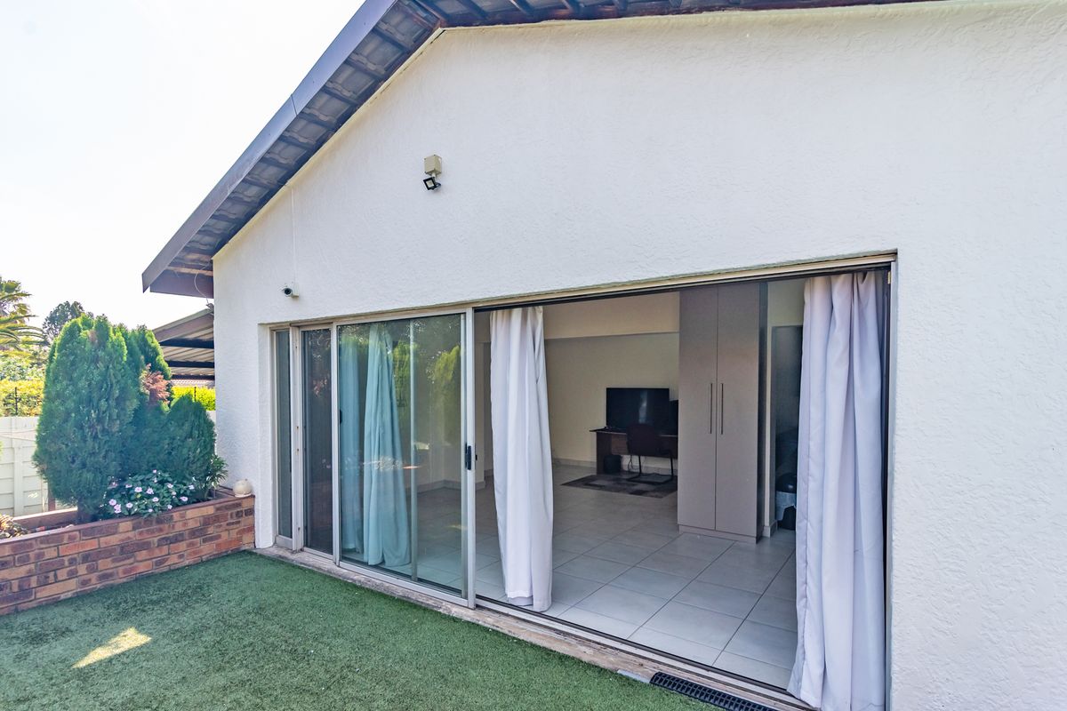 Rear view of the property featuring large sliding glass doors opening onto an artificial turf garden area with a brick planter.