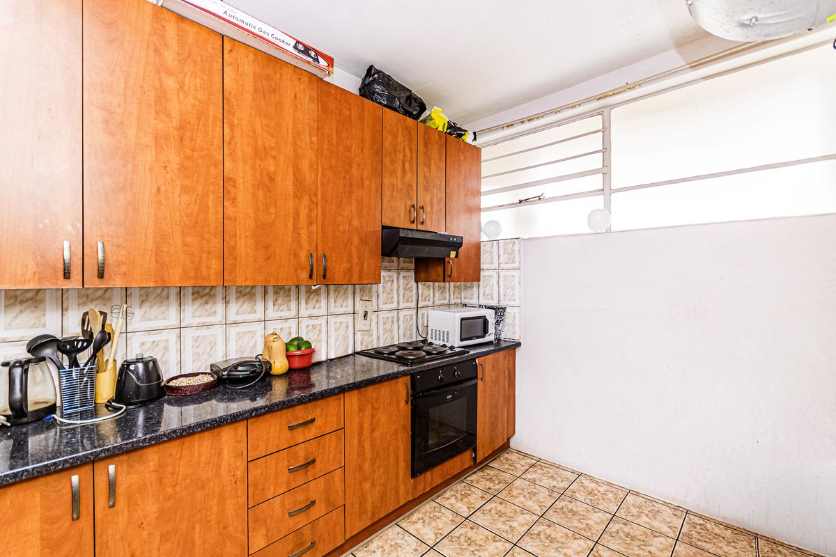 A functional kitchen featuring wood-look laminate cabinetry, granite countertops, built-in oven and hob, and tiled finishes throughout.