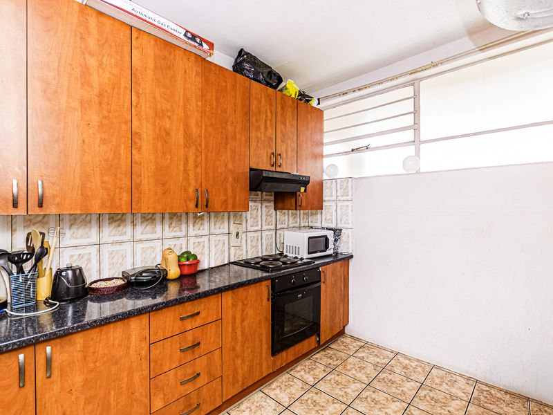 A functional kitchen featuring wood-look laminate cabinetry, granite countertops, built-in oven and hob, and tiled finishes throughout.