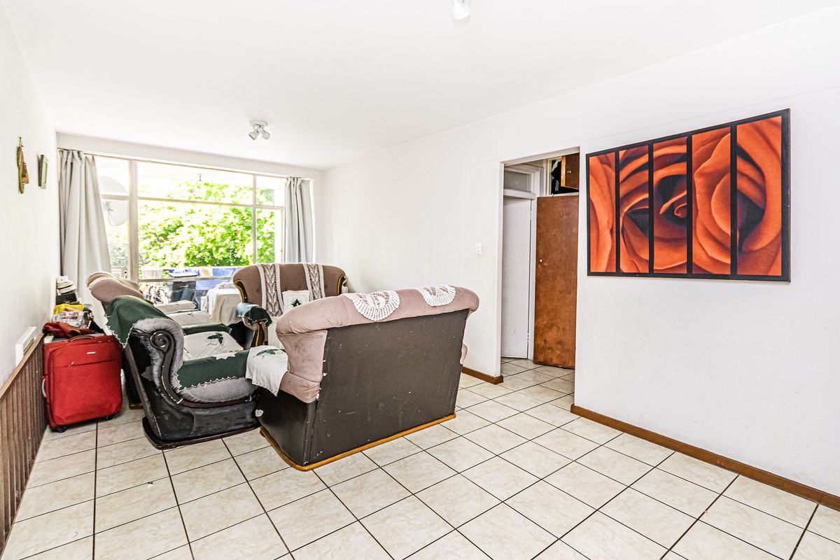 A living room area featuring tiled flooring and a large window providing natural light, with access to an adjacent room.