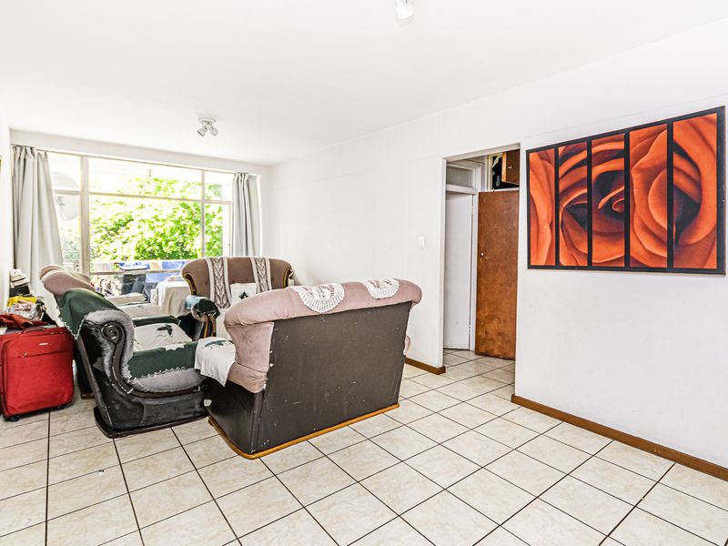 A living room area featuring tiled flooring and a large window providing natural light, with access to an adjacent room.