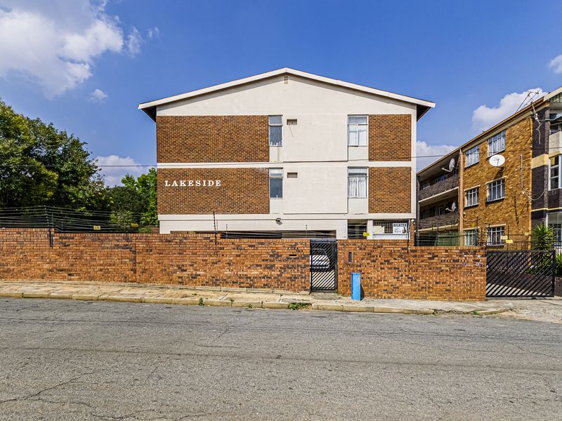 Front exterior view of the Lakeside apartment complex featuring a brick boundary wall, electric fencing, and secure gated access.