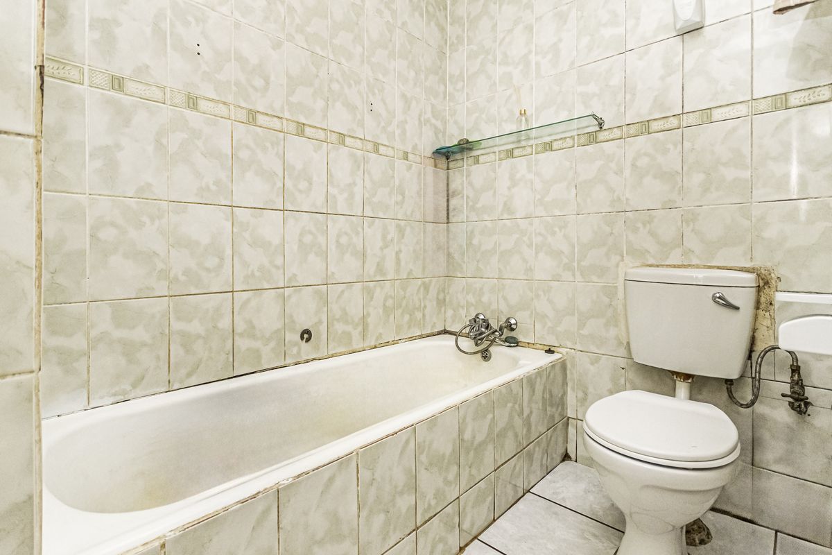 A dated bathroom featuring a bathtub, toilet, and full-height wall tiling. The space requires renovation to update the finishes and fixtures.