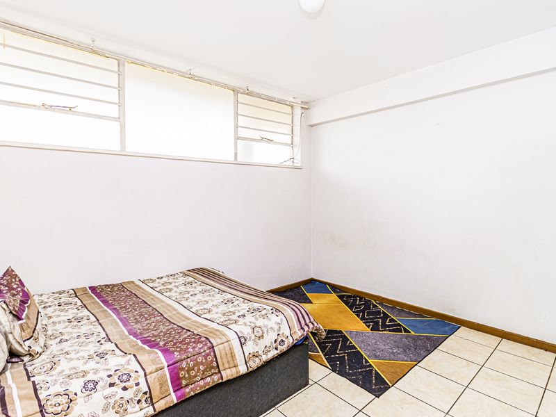 A bedroom featuring tiled flooring and high-level windows with security bars, offering a functional and bright living space.