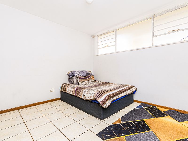 A bedroom featuring tiled flooring and louvre windows, requiring minor repairs to the flooring and electrical fixtures.