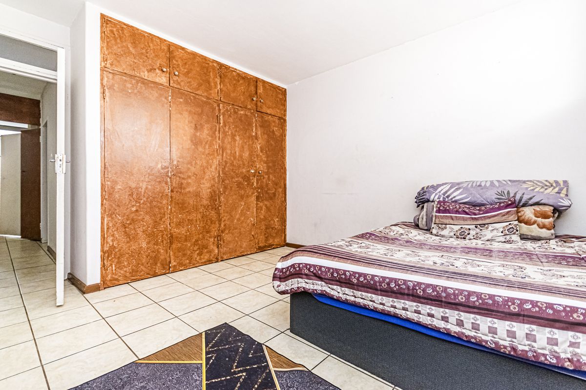 A bedroom featuring tiled flooring and large built-in cupboards with a dated finish, offering potential for modernization and aesthetic improvement.