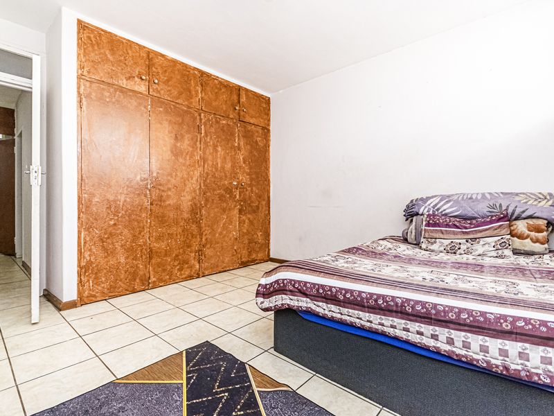 A bedroom featuring tiled flooring and large built-in cupboards with a dated finish, offering potential for modernization and aesthetic improvement.