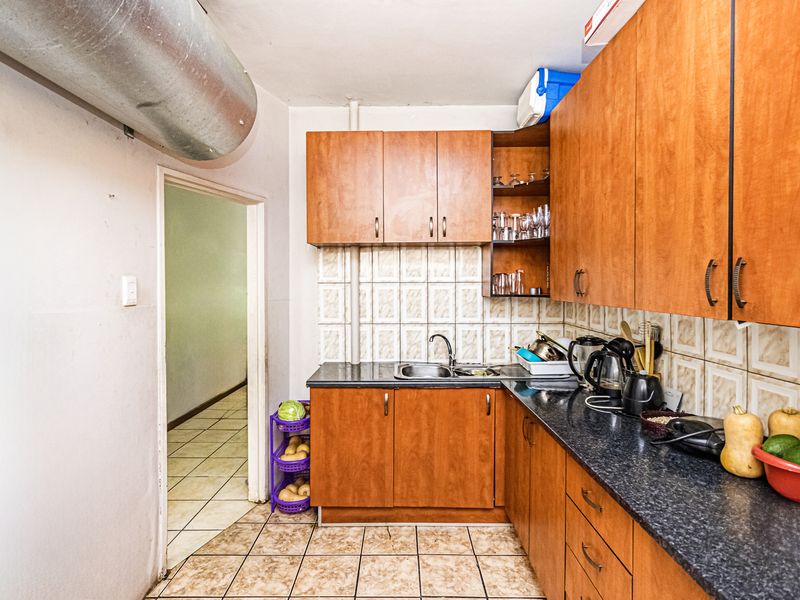 A functional kitchen featuring wood-look laminate cabinetry, dark countertops, tiled backsplash, and exposed industrial-style ventilation ducting.