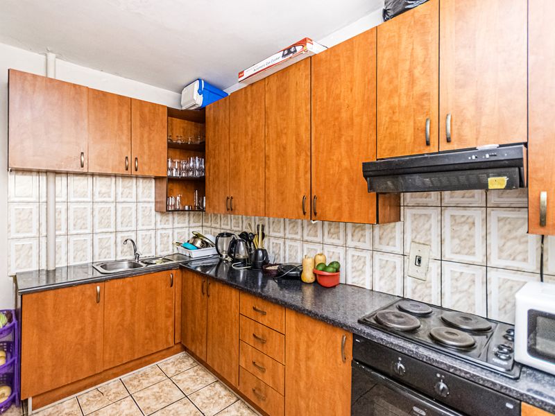 A functional kitchen featuring wood-tone laminate cabinetry, granite countertops, integrated electric hob and oven, and ceramic tiled splashbacks.