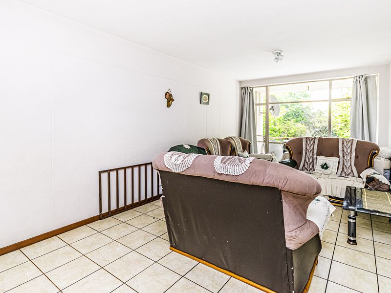 A living room featuring tiled flooring and a large window providing natural light and access to an outdoor area.