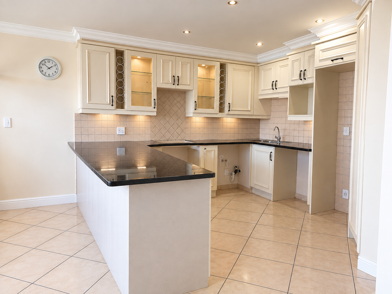 A clean, well-maintained kitchen featuring granite countertops, tiled backsplash, ample built-in cabinetry, and recessed lighting, offering a functional and bright workspace.