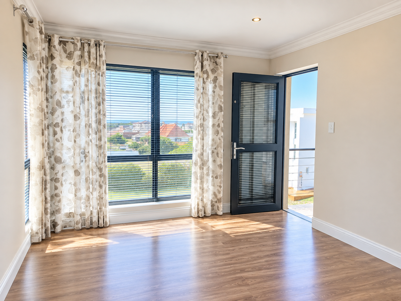 Bright and spacious bedroom featuring laminate flooring, recessed lighting, and direct access to a private balcony with scenic neighbourhood views.