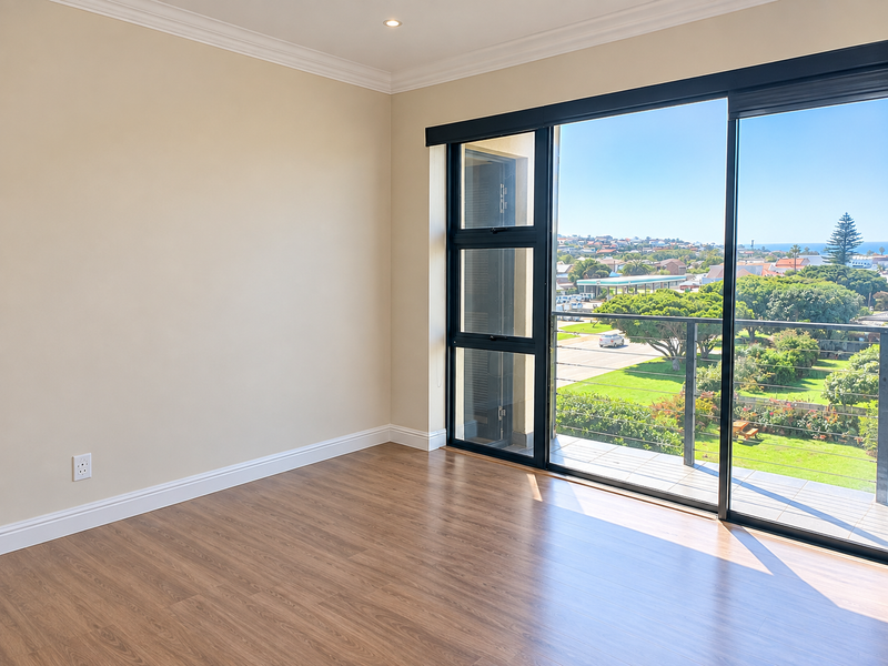 A bright, empty bedroom featuring modern laminate flooring, recessed lighting, and a large sliding glass door opening onto a private balcony with scenic views.