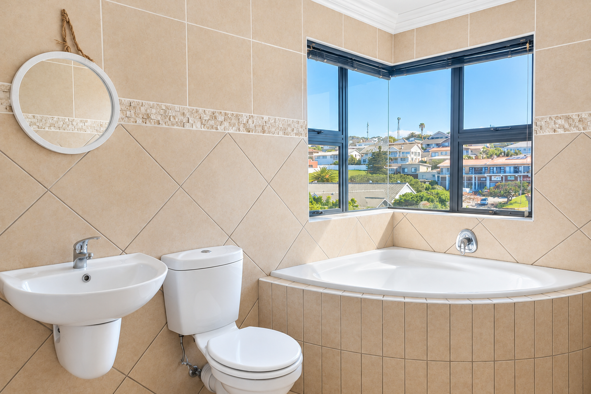 A bright, well-maintained bathroom featuring a corner bathtub, wall-mounted basin, and dual-flush toilet, complemented by neutral ceramic tiling and a scenic corner window.
