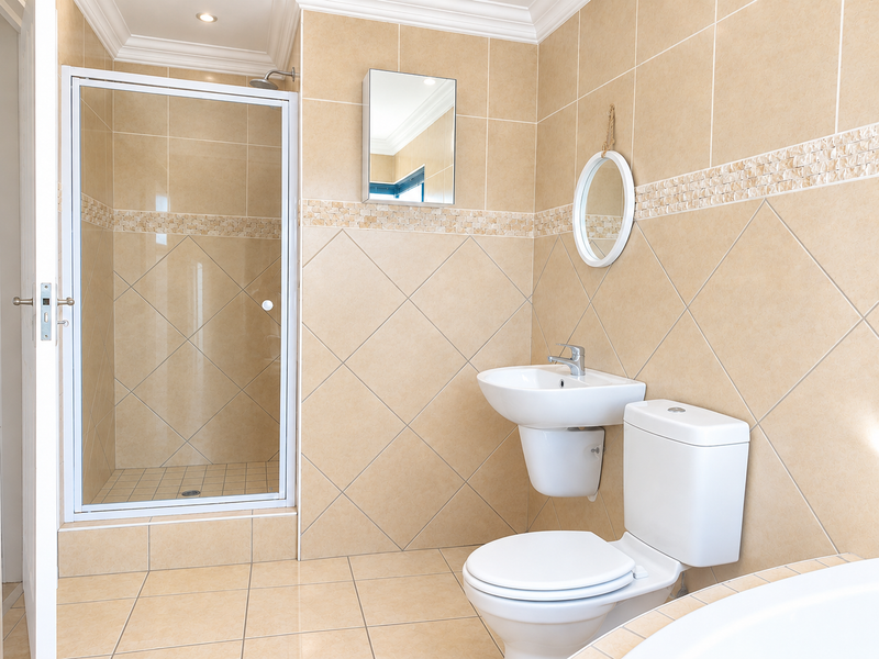 A clean, well-maintained bathroom featuring a glass-enclosed shower, wall-mounted basin, and toilet, finished with neutral beige wall and floor tiles.