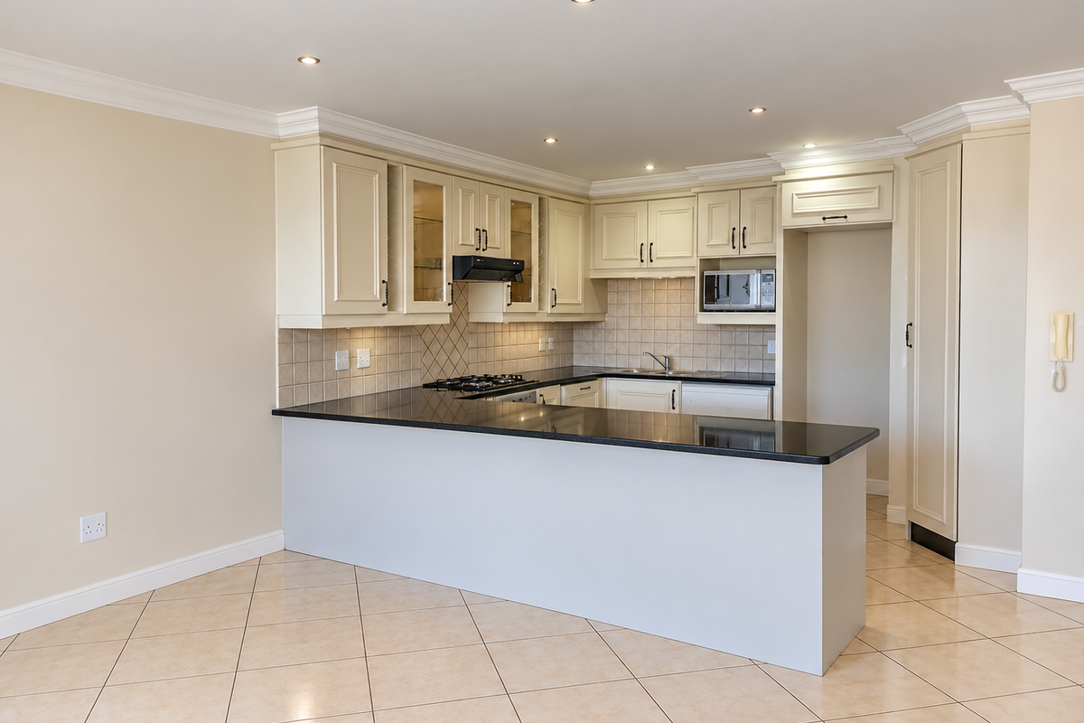Spacious open-plan kitchen featuring cream cabinetry, granite countertops, built-in appliances, and tiled flooring, offering a clean and functional layout.