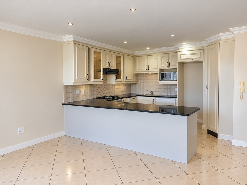 Spacious open-plan kitchen featuring cream cabinetry, granite countertops, built-in appliances, and tiled flooring, offering a clean and functional layout.