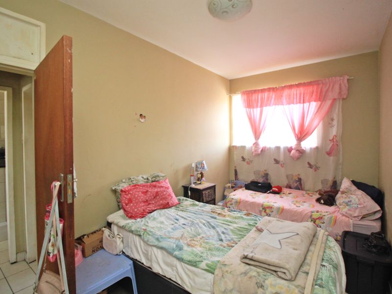 A bedroom featuring a window and standard finishes, requiring cosmetic updates to the walls and general maintenance.