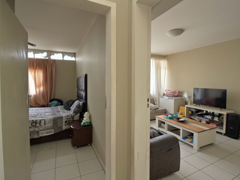 A view from a hallway looking into a bedroom and a living area, featuring neutral wall tones and consistent tiled flooring throughout.
