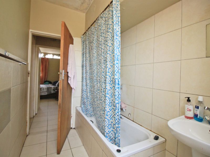 A functional bathroom featuring a bathtub with shower curtain, pedestal basin, and tiled finishes, showing signs of ceiling wear requiring maintenance.