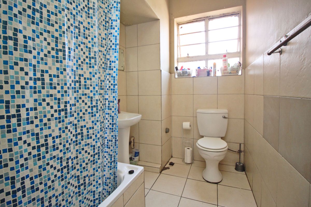 A functional bathroom featuring a pedestal sink, toilet, and tiled finishes, requiring cosmetic updates to improve its overall condition and aesthetic appeal.